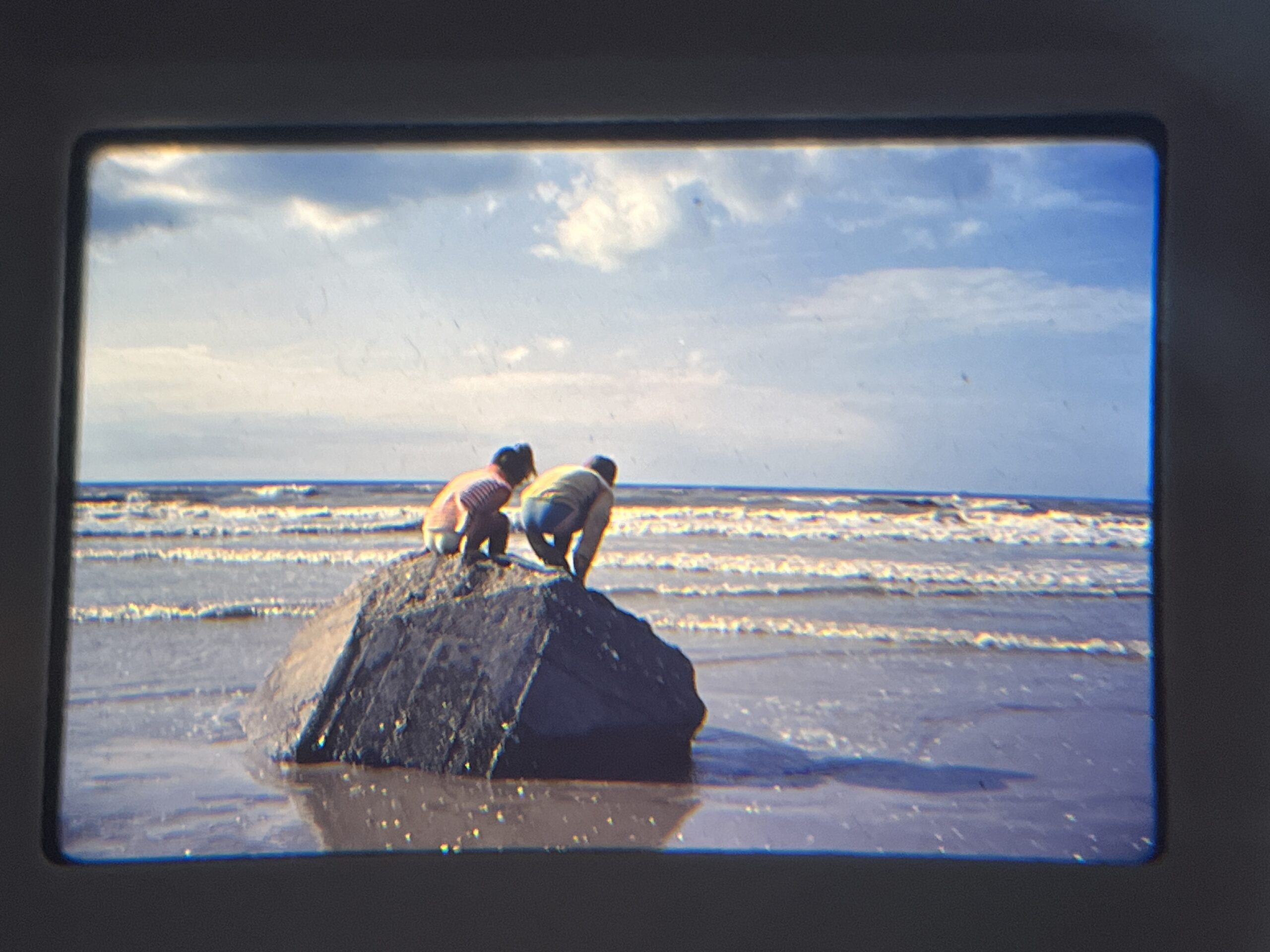 Twee kinderen op een rots in de zee, nieuwsgierig naar beneden kijkend